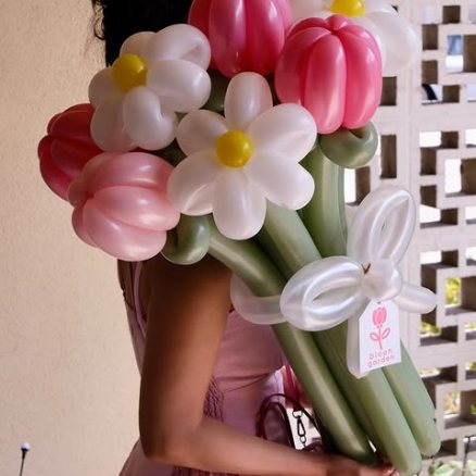 A large bouquet of red, pink and white balloon daisies and tulips held against a pink dress.